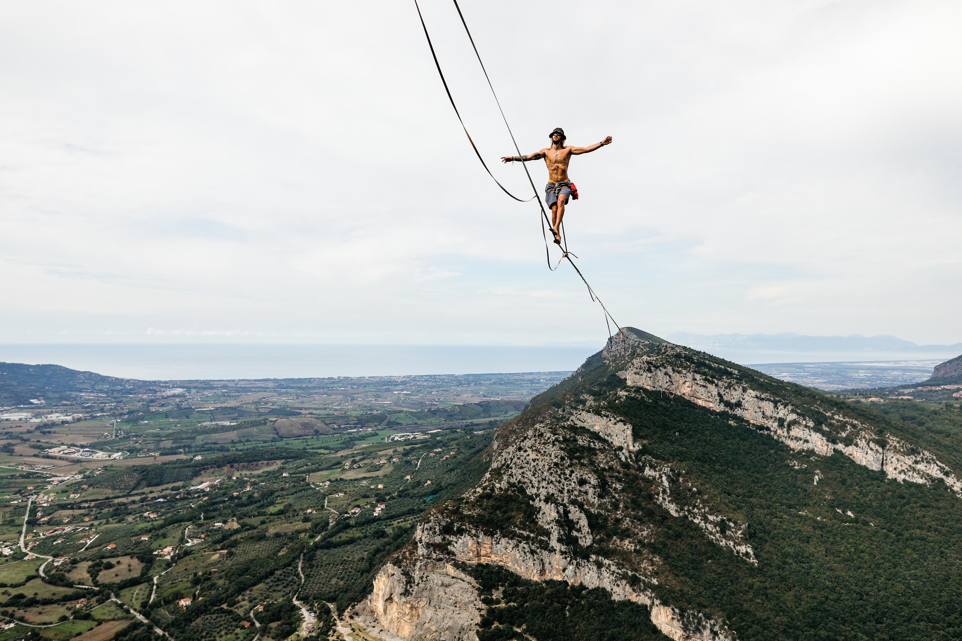Alessandro in equilibrio su una highline sospesa sopra una vallata, con il mare all'orizzonte